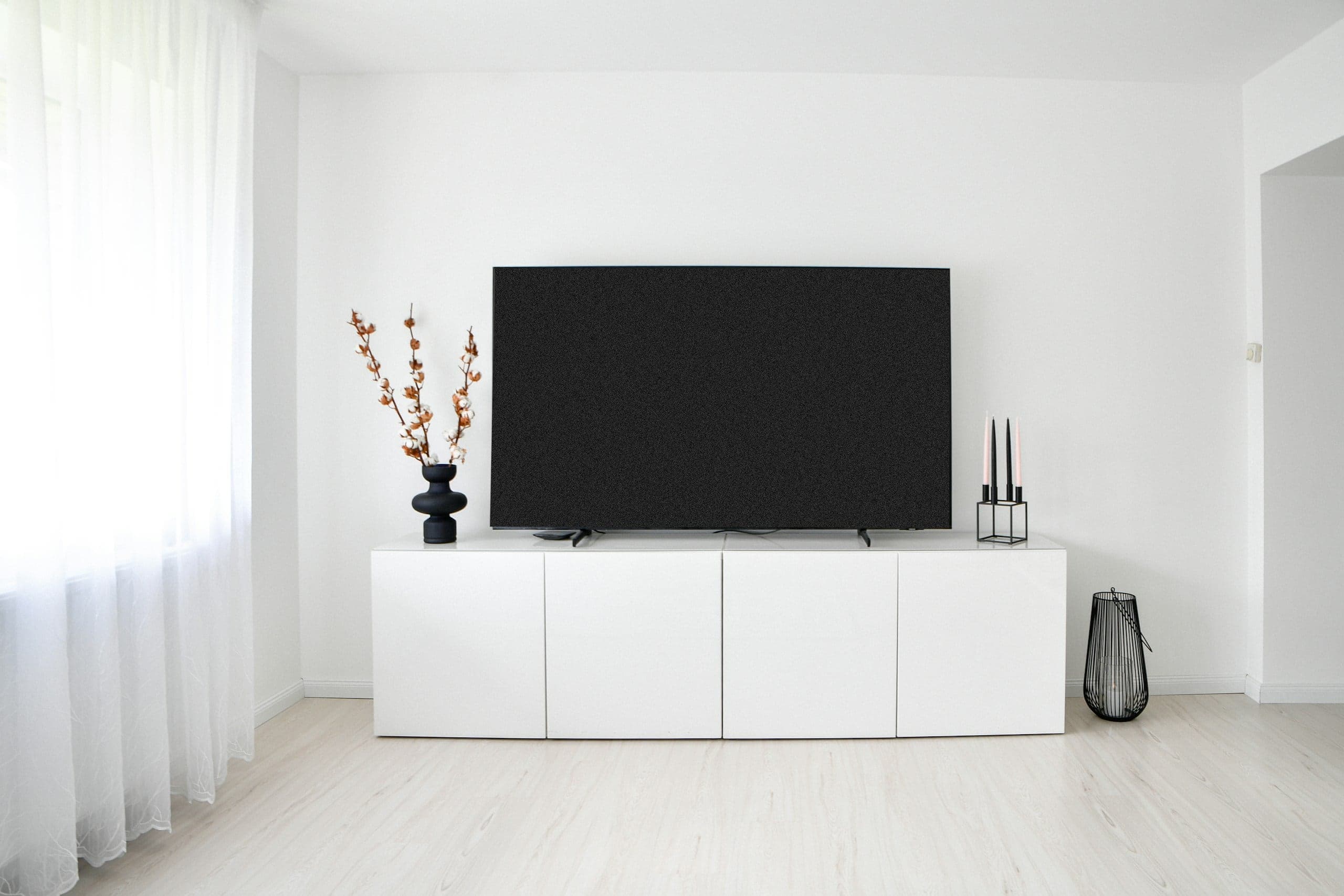 Heller, minimalistischer Wohnraum: ausgeschalteter Fernseher auf weißem Sideboard, daneben Vorhänge im Tageslicht