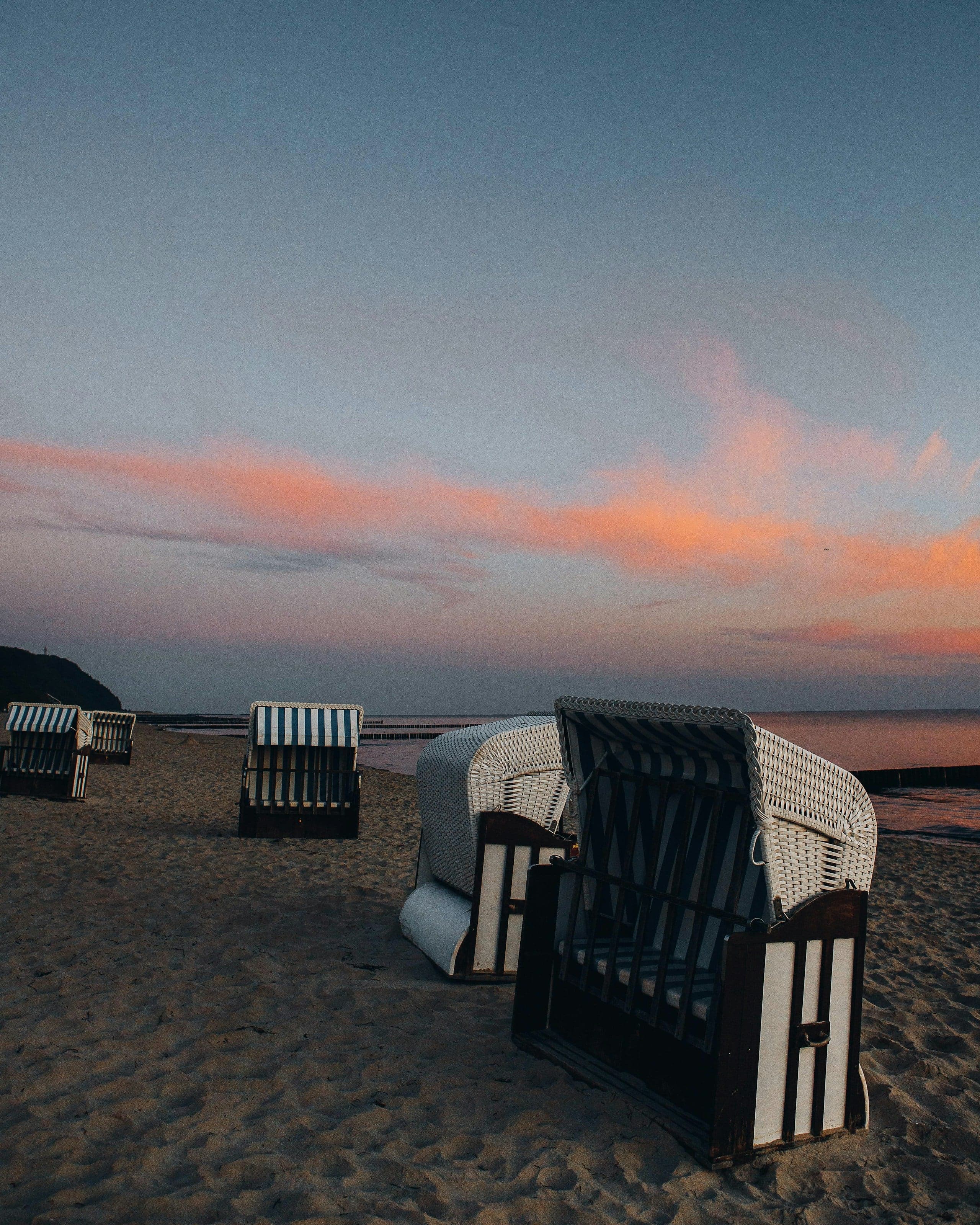 Leere Strandkörbe am Ostseestrand in der Dämmerung, im Hintergrund Buhnen und ruhiges Meer