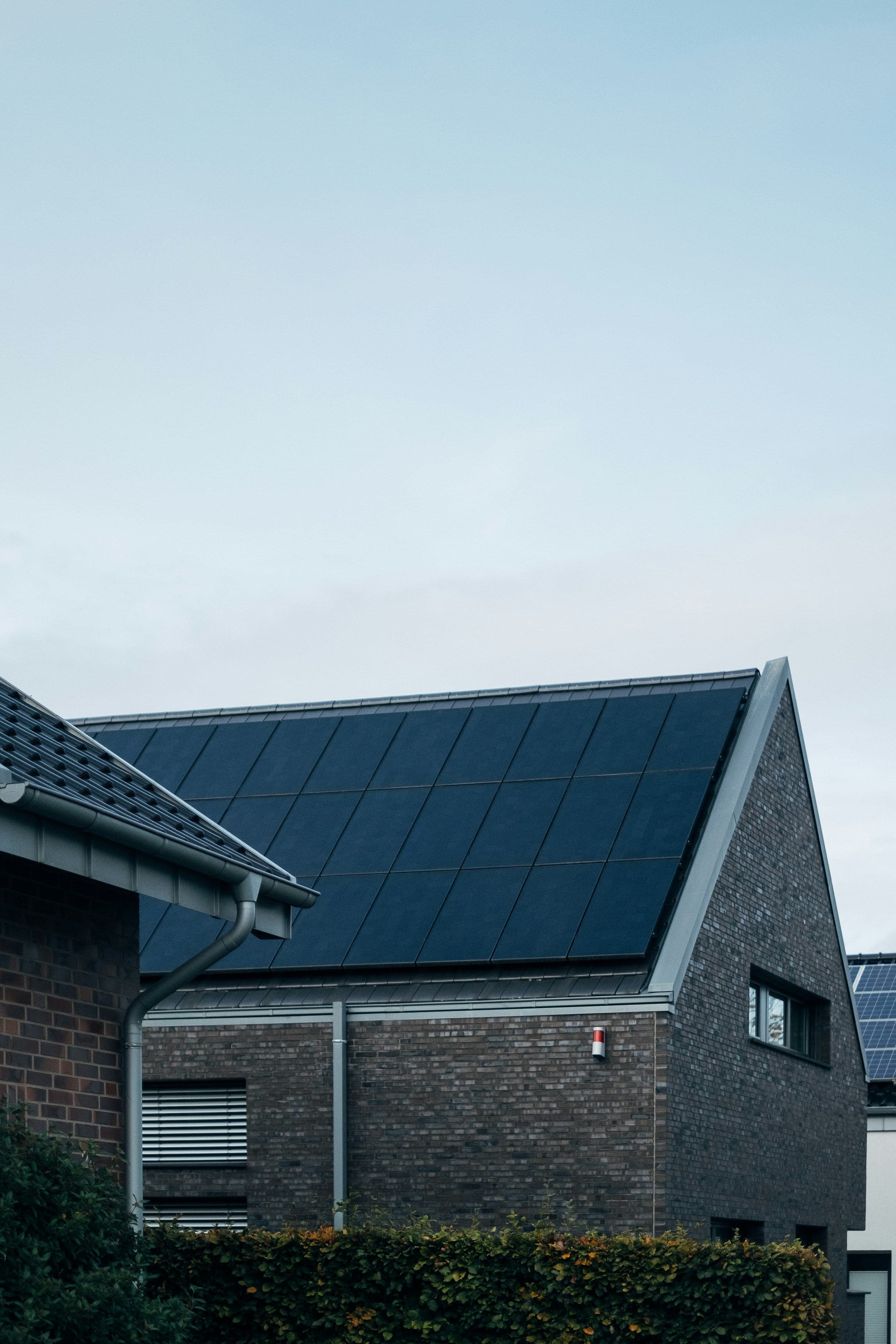 Einfamilienhaus aus dunklem Klinker mit Solarmodulen auf dem Satteldach unter hellem, weitem Himmel