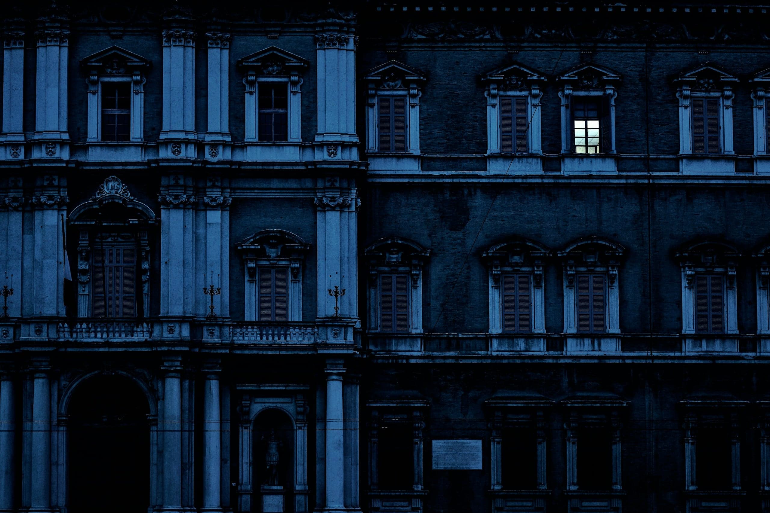 Dunkle historische Palastfassade zur blauen Stunde, nur ein einziges Fenster ist erleuchtet